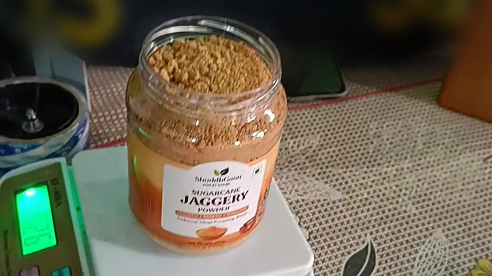 A jar of ShuddhGaon jaggery powder being weighed on a packing scale